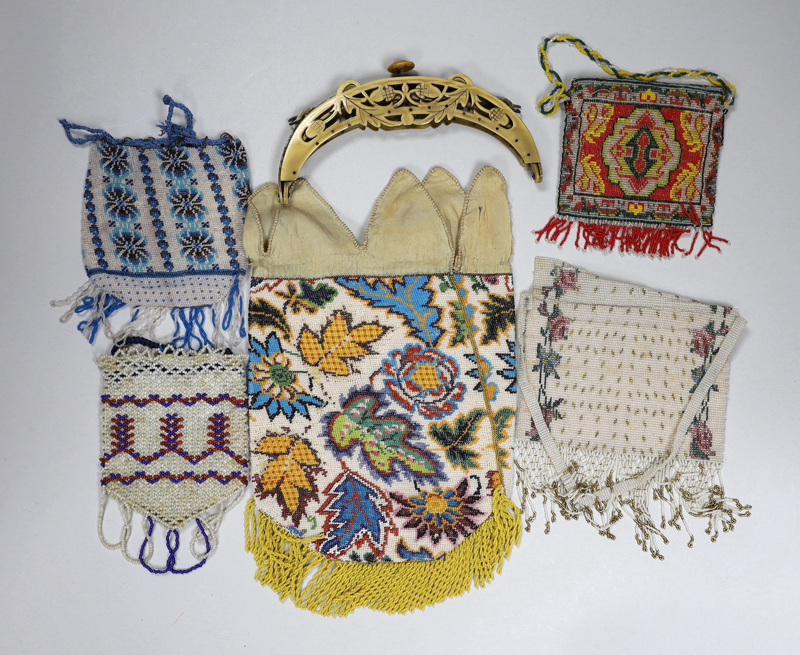 A 19th century ornately multicoloured beaded bag with a bead fringe, two smaller similar beaded purses a later coloured cut steel evening bag and a 1920’s Bakelite frame (6)